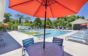 A red umbrella is over a round table with blue chairs.
